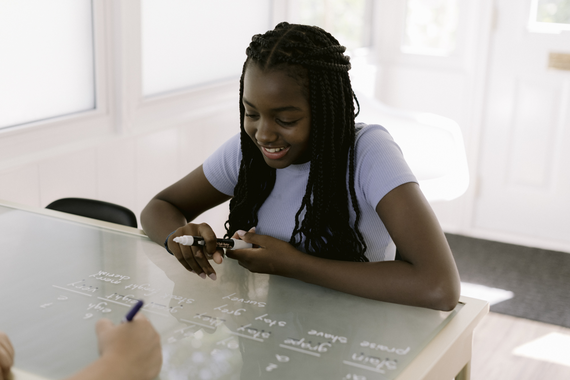 A learner smiling while writing words on a glass board during a Clubhouse tutoring session